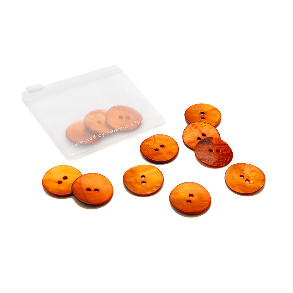 Neun orange-braune Alexandra Renke Akoya Muschelknöpfe mit je zwei Löchern und glänzender Oberfläche sind neben einem durchscheinenden Beutel auf weißem Grund angeordnet.