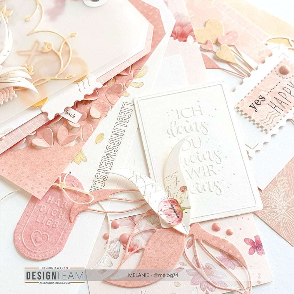 Ein flaches Layout aus rosa und weißen handgefertigten Karten, Anhängern und Papierbasteleien mit Blumen- und Herzmotiven, die mit Alexandra Renke Designpapieren hergestellt und mit ihren Stanzsystemen für komplizierte Feinarbeiten veredelt wurden.