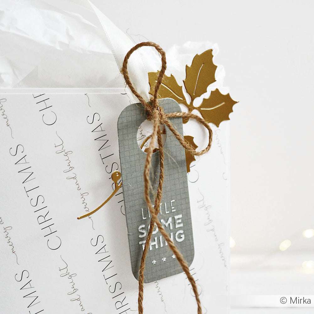 Weiße Geschenktüte von Alexandra Renke mit dem Text "Merry and Bright Christmas", braunem Garn, goldener Stechpalme und einem "Little Something"-Anhänger - hergestellt aus Designpapier und mit einem Prägefolder für ein elegantes Finish veredelt.