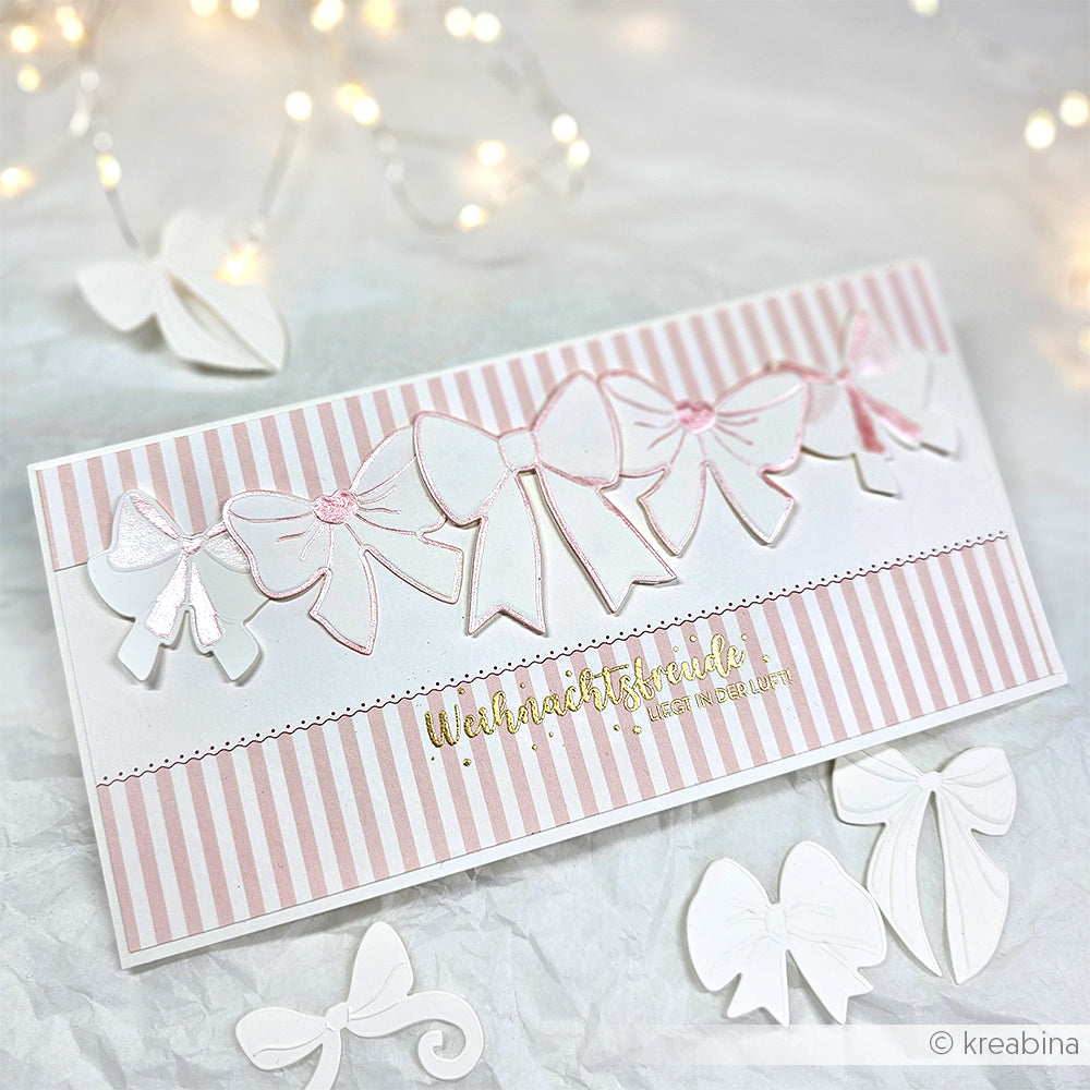 Eine rosa-weiß gestreifte Karte mit dem Schneide- und Prägefolder Alexandra Renke Schleifenpracht mit Papierschleifen, goldenem Weihnachtsfreude-Text und weißen Ornamenten - ideal, um Ihre Lieblingstechniken mit Stanzsystemen hervorzuheben.