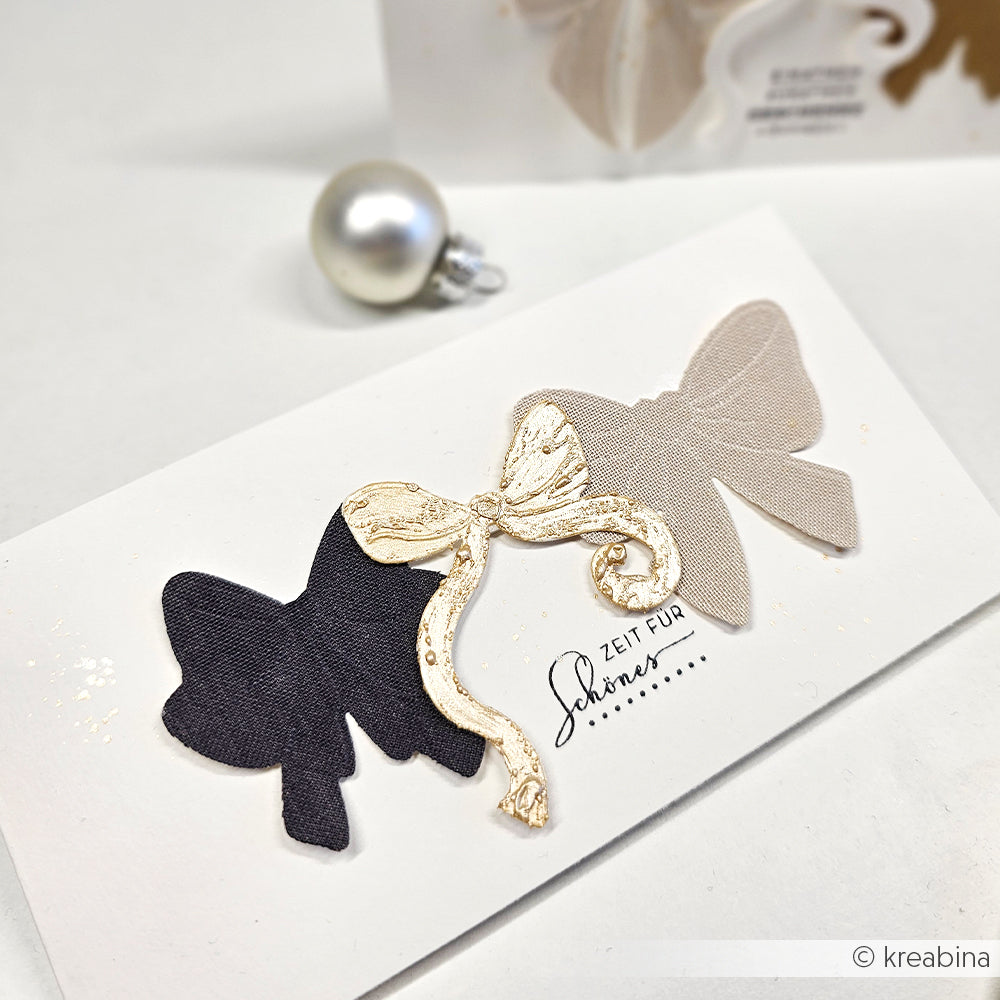 Handgefertigte Karte mit schwarzen und beigen Schleifen und einem goldenen Akzent auf Weiß, hergestellt mit dem Alexandra Renke Schleifenpracht Cut & Emboss Folder für elegante, präzise Details.