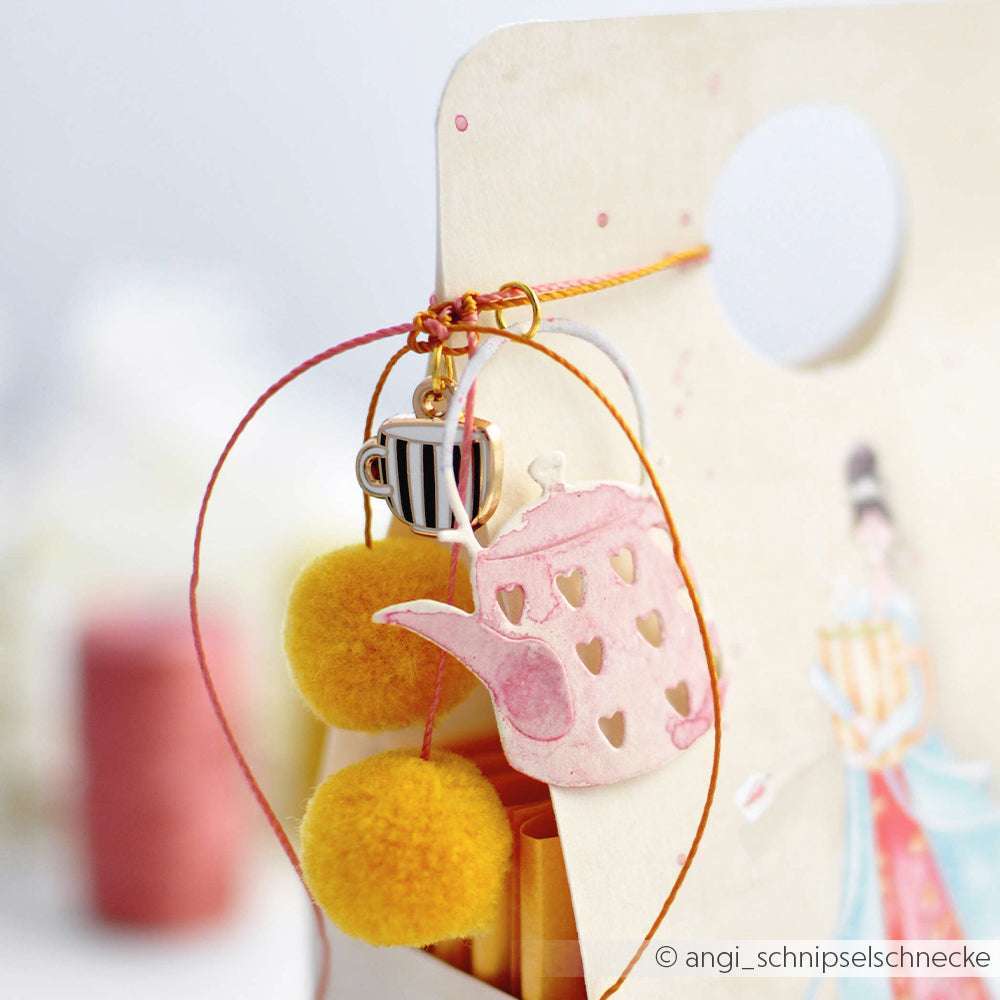 Geschenkanhänger von Alexandra Renke mit einem rosa Teekannenausschnitt, gelben Bommeln und einem gestreiften Teetassenanhänger mit orangefarbener Schnur - ideal für Charms Kaffeezeit oder als Anhänger Buchbinden in Ihrem nächsten Kreativprojekt.