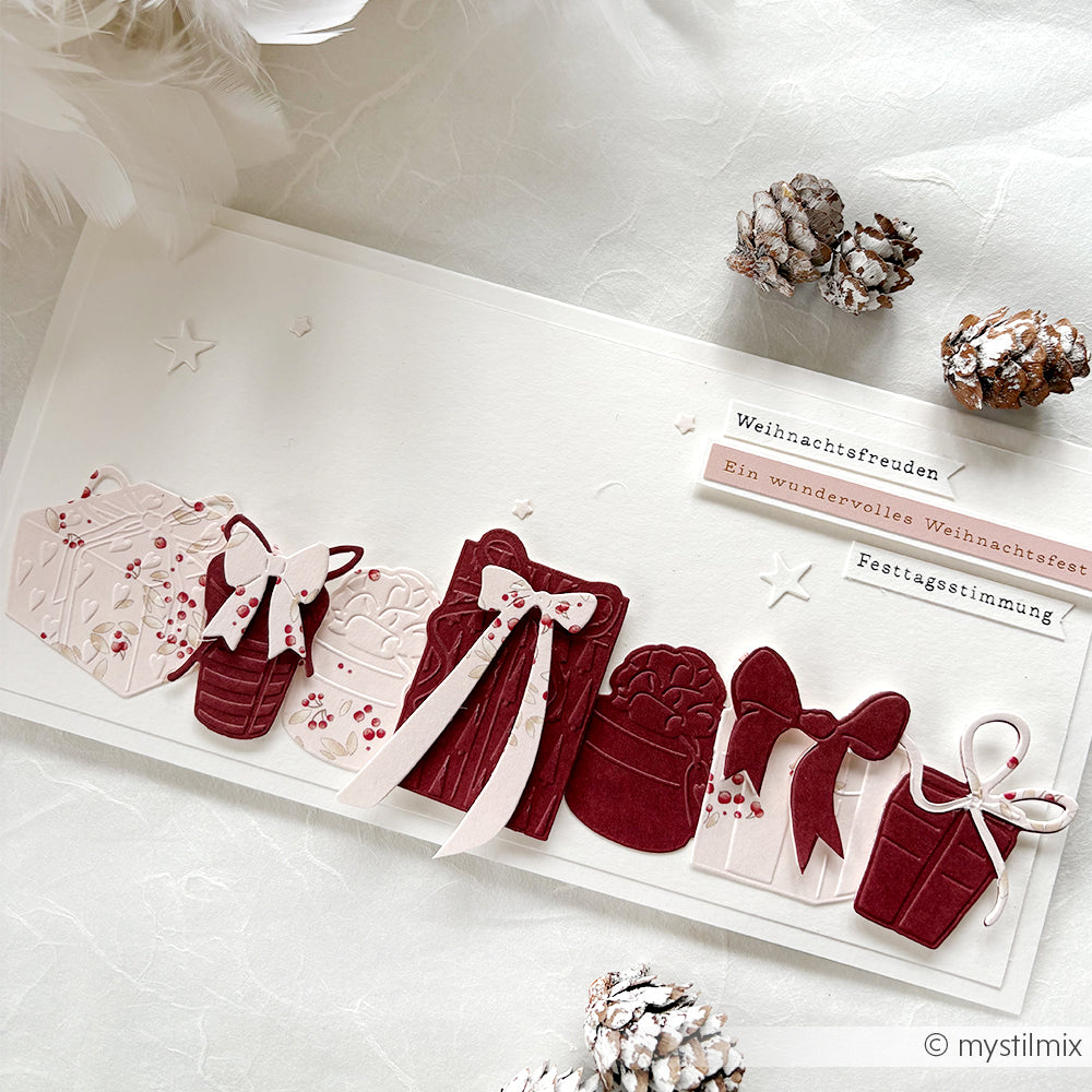 Handgefertigte Weihnachtskarte mit Papierausschnitten von Geschenken, Schleifen, Fäustlingen, Tannenzapfen und festlichen deutschen Texten, hergestellt mit Alexandra Renke Stanzsystemen für präzise Formen und Designpapieren für eine einzigartige Note.