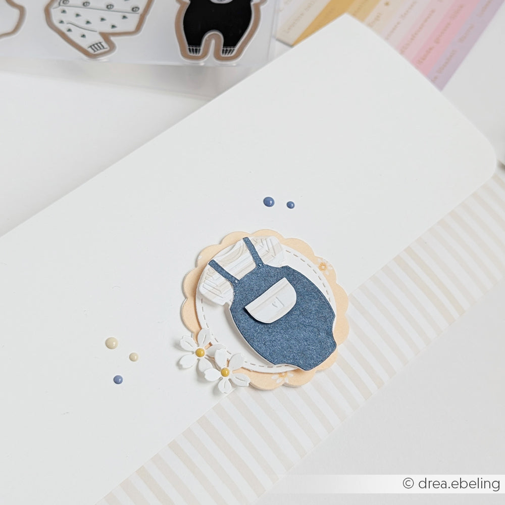 Karte mit einer Papierverzierung aus blauen Overalls, Blumen und Perlen auf einem gestreiften weißen Hintergrund, gestaltet mit Alexandra Renke Designpapieren und einem Cut & Emboss Folder für zusätzliche Textur.