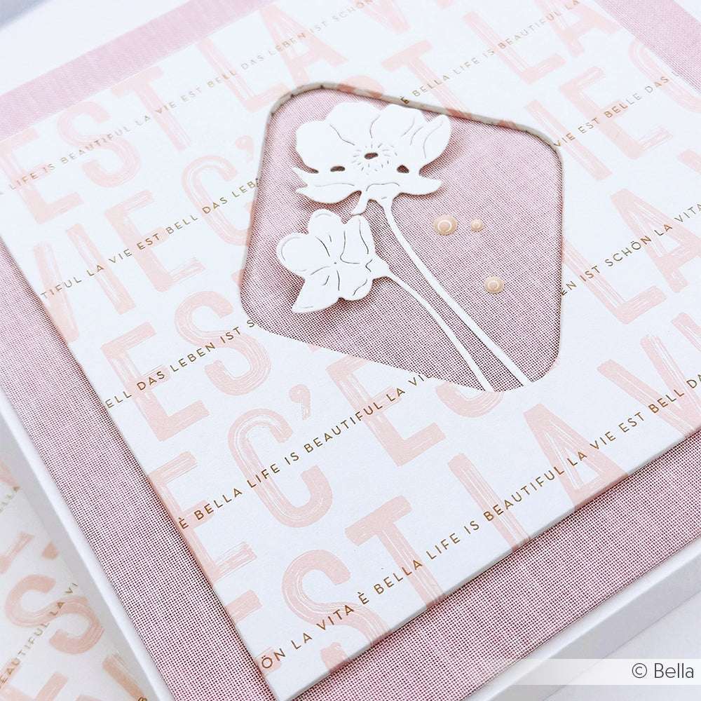 Eine rosa-weiße Alexandra Renke-Grußkarte mit geprägten Blumen und "Das Leben ist schön" in mehreren Sprachen, hergestellt mit PAPPcuts-Techniken für eine besondere Note.