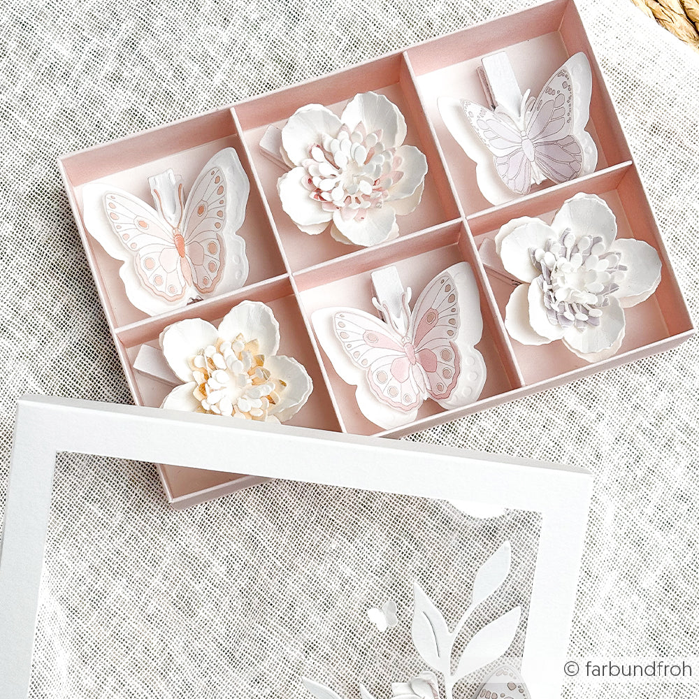Schachtel mit sechs Fächern, die jeweils einen kunstvoll gearbeiteten Papier-Schmetterling oder eine Blume in zarten Pastelltönen enthalten – meisterhaft gefertigt mit Stanzsystemen von Alexandra Renke und inspiriert vom verspielten Charme von „Schmetterlingsfreuden“.