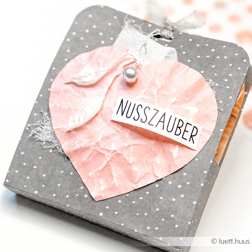Graue gepunktete Geschenkbox von Alexandra Renke mit rosa PAPPcut Herz, weißem Band, Perle und Nusszauber-Etikett - ideal zum Buchbinden oder kreativen Verpacken von Geschenken.