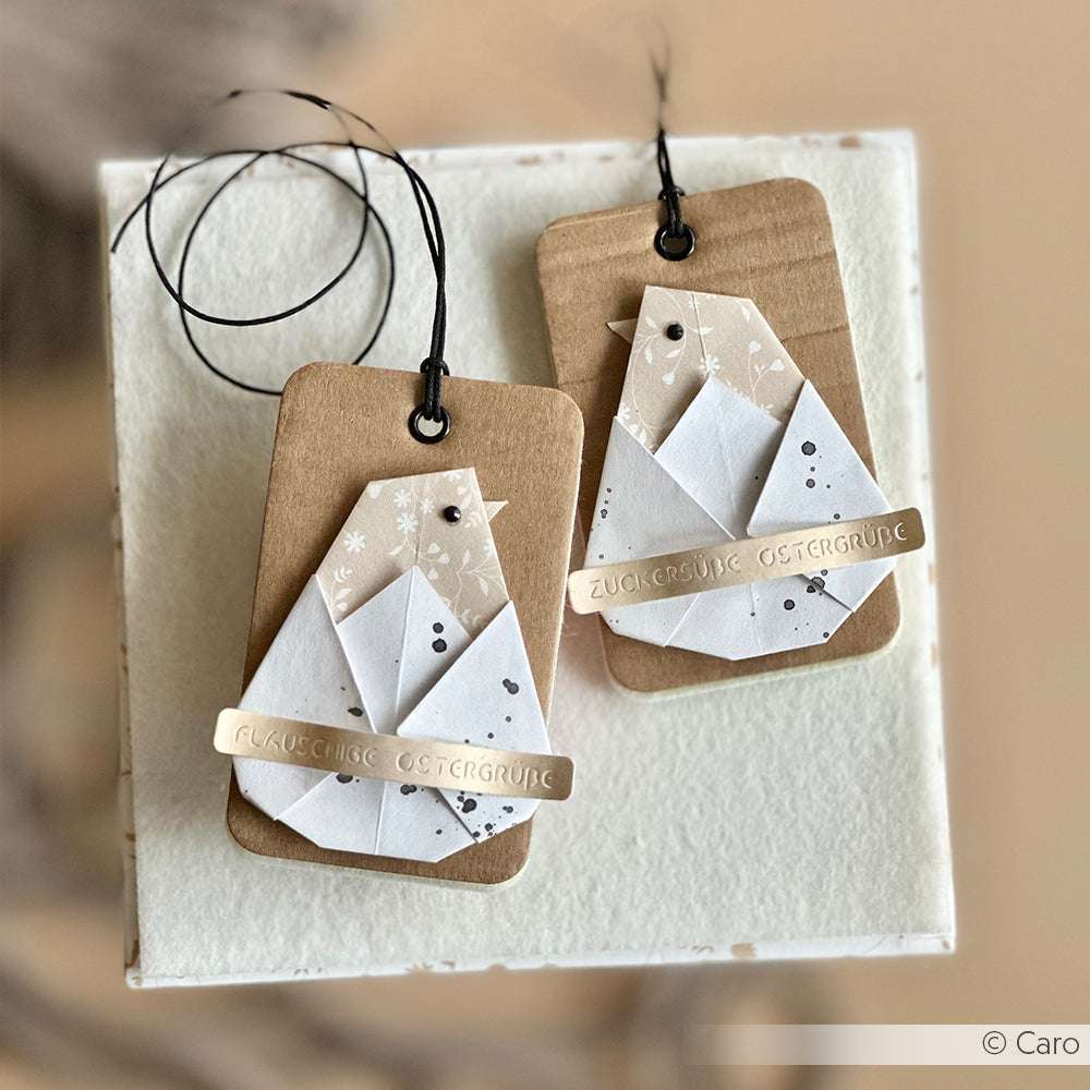 Zwei handgefertigte Geschenkanhänger mit Origami-Vögeln, hergestellt mit PAPPcuts®-Techniken von Alexandra Renke, verziert mit schwarzer Schnur und deutschen Weihnachtsgrüßen.