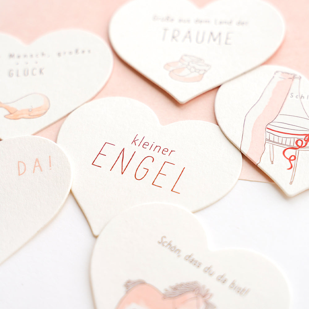 Mehrere weiße, herzförmige Karten von Alexandra Renke mit deutschem Text und zartrosa Motiven - perfekt als Bastelmotiv oder zur Verwendung mit Transferfolie - sind auf hellem Hintergrund angeordnet.