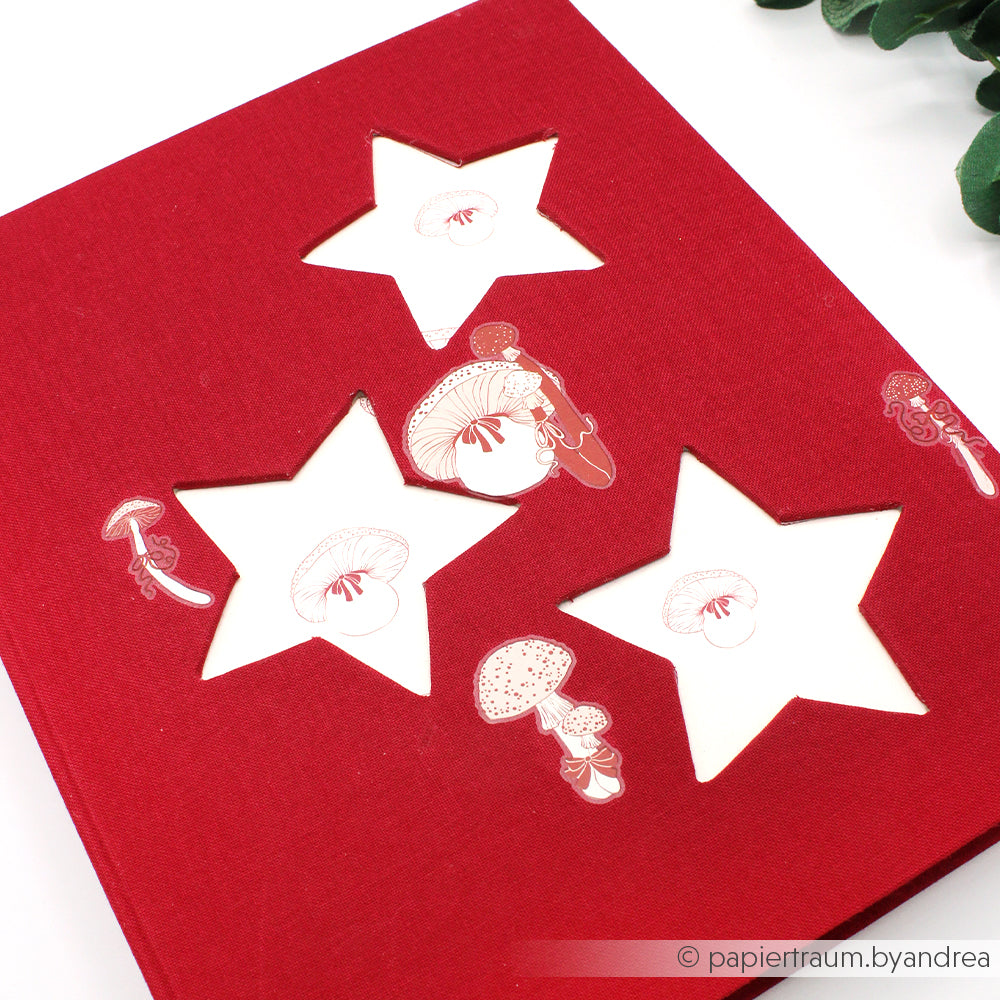 Rotes Notizbuch von Alexandra Renke mit sternförmigen PAPPcut-Ausschnitten und skurrilen Pilzillustrationen in Buchbindetechnik auf weißem Untergrund.