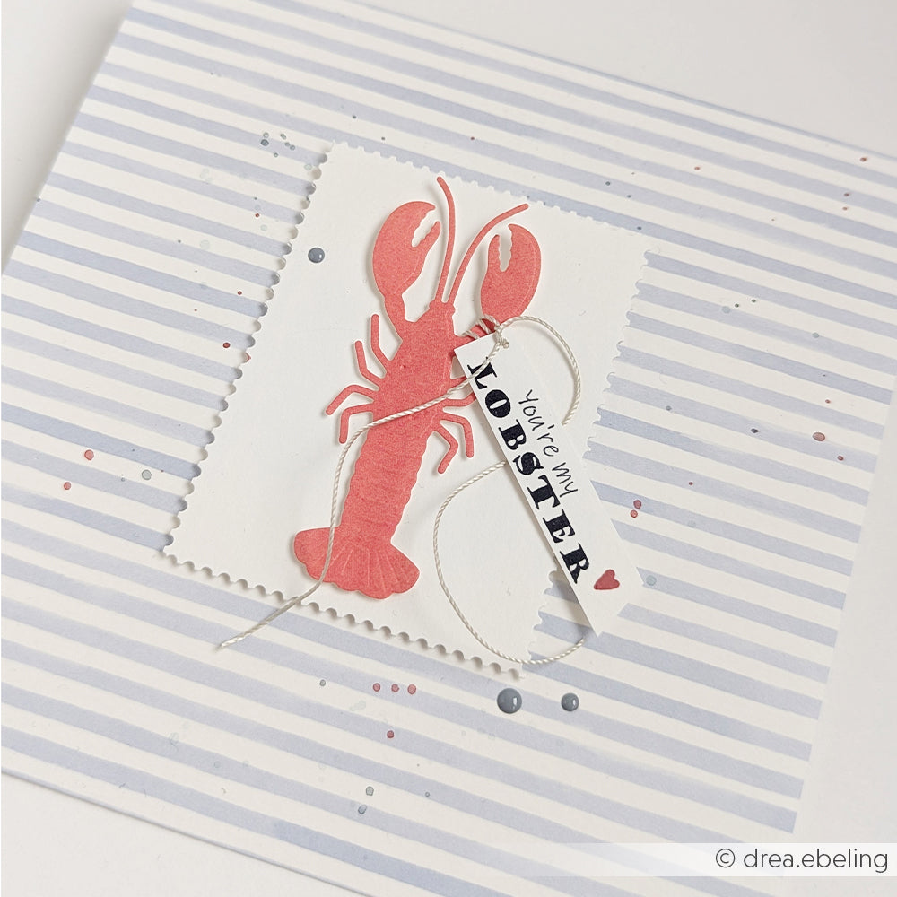 Handgefertigte Karte von Alexandra Renke mit einem roten Hummer und einem Anhänger mit der Aufschrift „You’re my lobster“ auf gestreiftem Hintergrund, gestaltet mit Stanzsystemen und einer Präge- und Stanzschablone für zusätzliche Details – perfekt für Fans maritimer Genüsse.