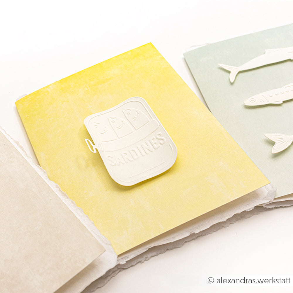 Drei pastellfarbene Karten von Alexandra Renke, darunter eine mit einer Sardinendosen-Illustration, sind auf weißem Hintergrund abgebildet - ideal, um Ihren maritimen Genuss mit einem Stanzsysteme Cut & Emboss Folder hervorzuheben.