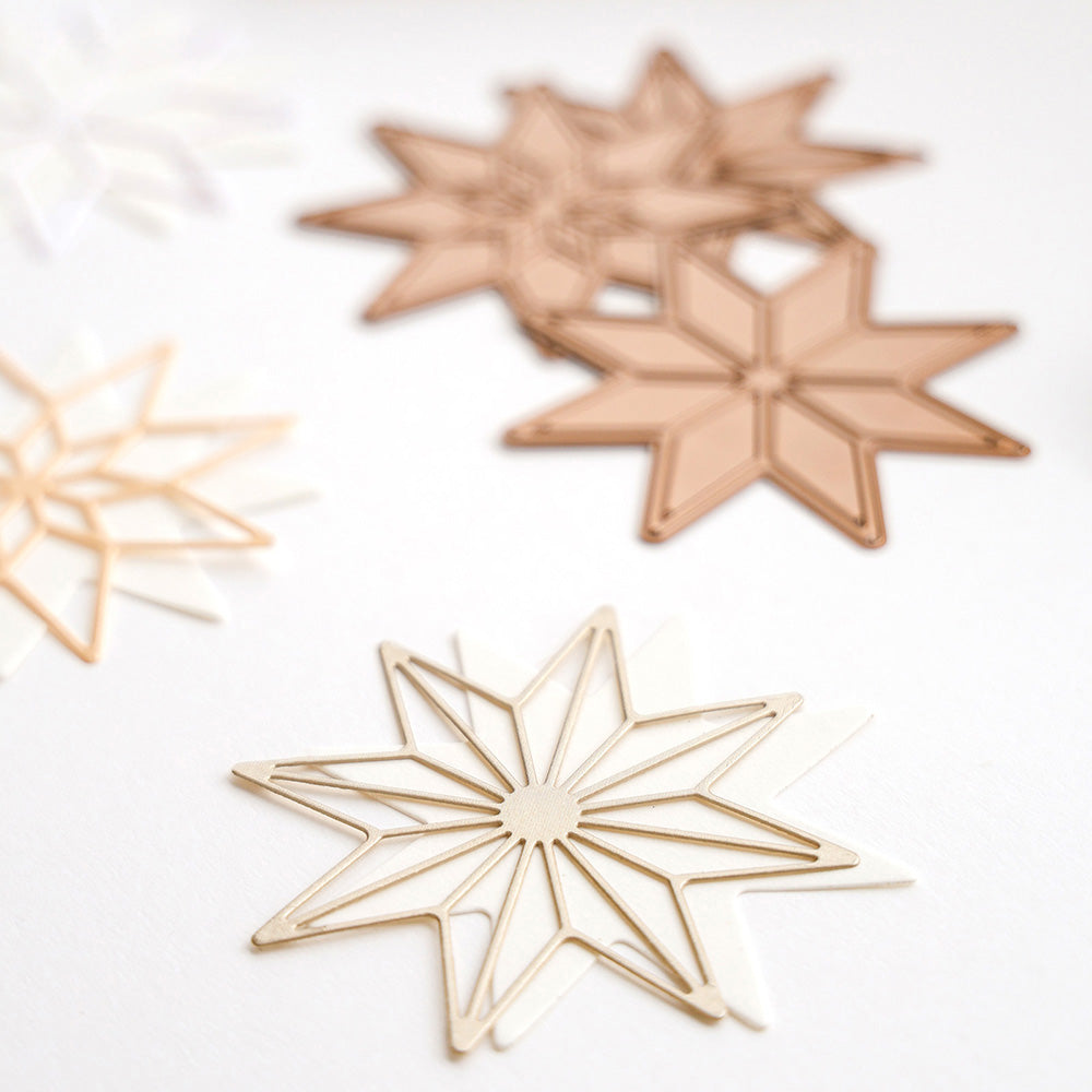 Alexandra Renke metallische sternförmige Büroklammern in Gold und Bronze, inspiriert von PAPPcut Achterstern, sind auf einer weißen Oberfläche angeordnet - perfekt zum Buchbinden oder Organisieren von Dokumenten mit Stahlbandstanzen Präzision.