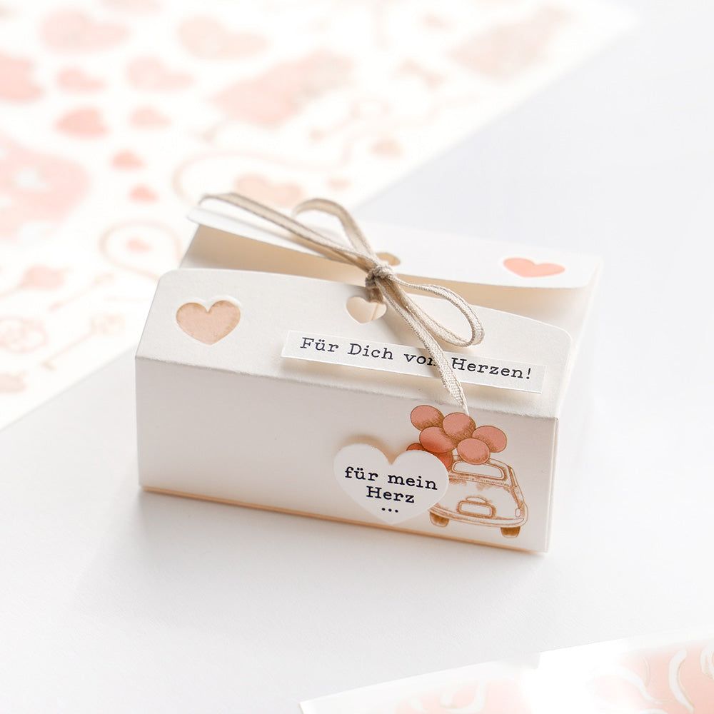 Die cremefarbene Geschenkbox von Alexandra Renke, verziert mit Herzmotiven, Rankenschleife und deutschen Botschaften - ideal für Bastelprojekte oder als Geschenk für einen besonderen Menschen.