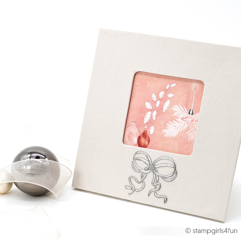 Quadratische weiße Weihnachtskarte von Alexandra Renke mit rosa Fenster, floralem Schablonendesign und silberner Schleife; daneben ein Ornament - ideal für Papierprojekte.