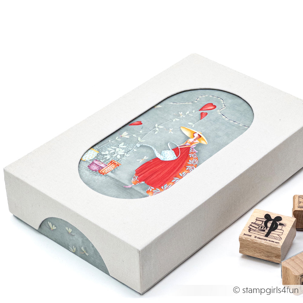 Weiße Schachtel mit ovalem Fenster zeigt das skurrile Alexandra Renke PAPPcuts-Kunstwerk eines Mädchens in Rot; Buchbinden Holzstempel liegen daneben.