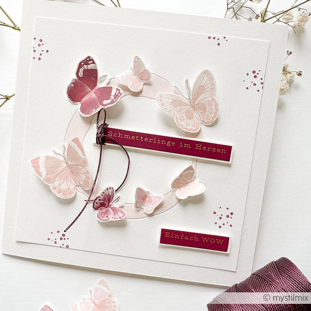 Eine handgefertigte Karte von Alexandra Renke mit rosafarbenen Schmetterlingen, weinroten Etiketten und dem deutschen Text "Schmetterlinge im Herzen" und "Einfach WOW", akzentuiert mit Rub-On Motiven von Rub-On Florales Fotoatelier für eine elegante Note.