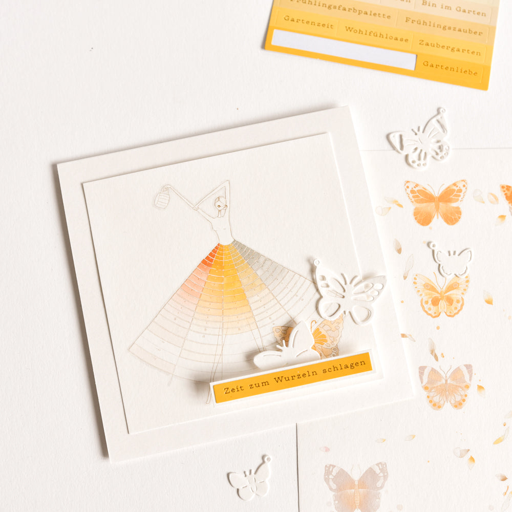 Eine quadratische Karte von Alexandra Renke mit einer stilisierten Tänzerin, orange-gelben Farbverläufen, Schmetterlingsausschnitten und "Zeit zum Wurzeln schlagen" - ideal für Bastelprojekte oder in Kombination mit Transferfolien für kreatives Flair.