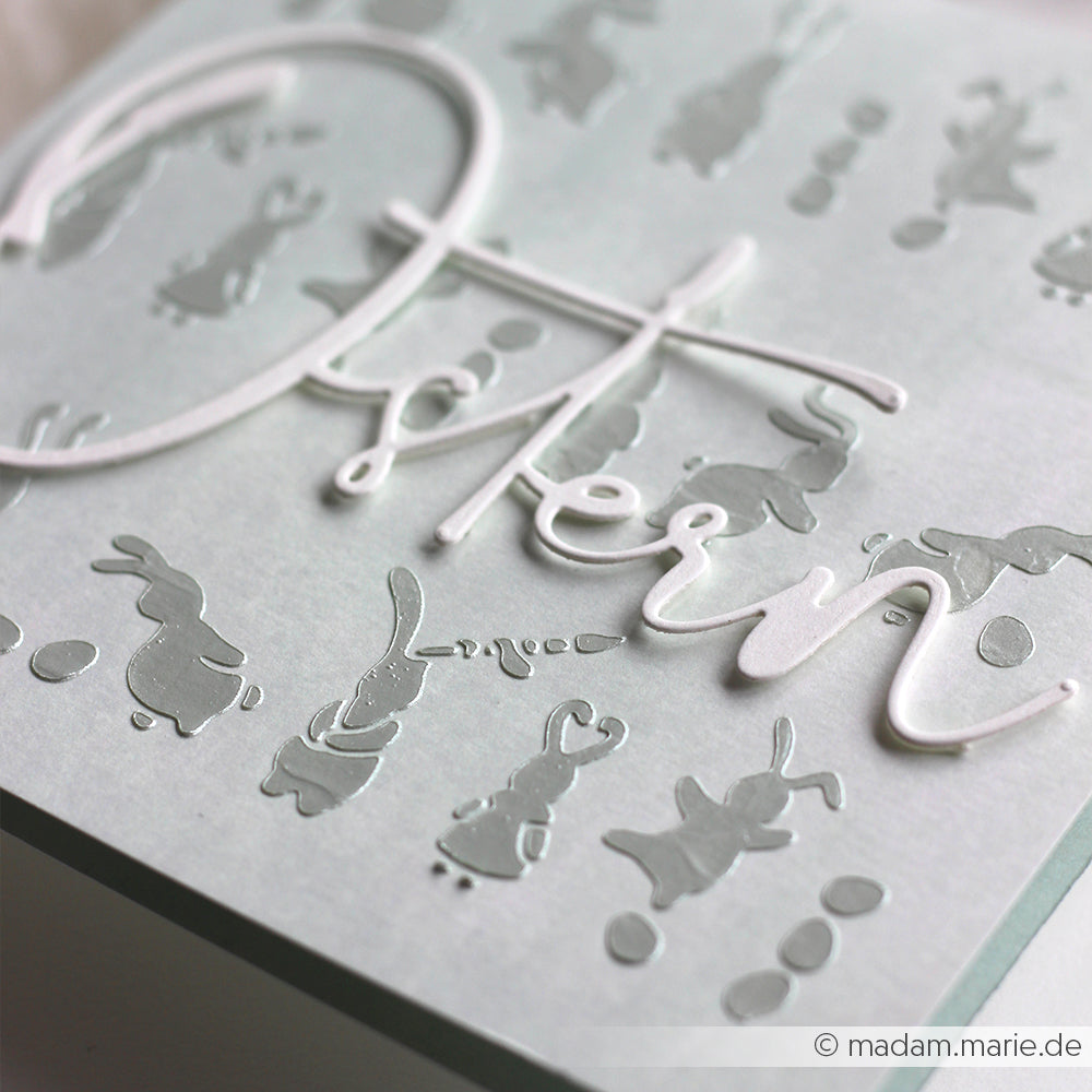 Nahaufnahme einer Karte von Alexandra Renke mit silbernen Hasen, Ostereiern und "Ostern" in weißer Schrift - eine großartige Inspiration für Papierprojekte oder die Verwendung von Stencil-Musterstreifen in Ihren eigenen handgefertigten Designs.