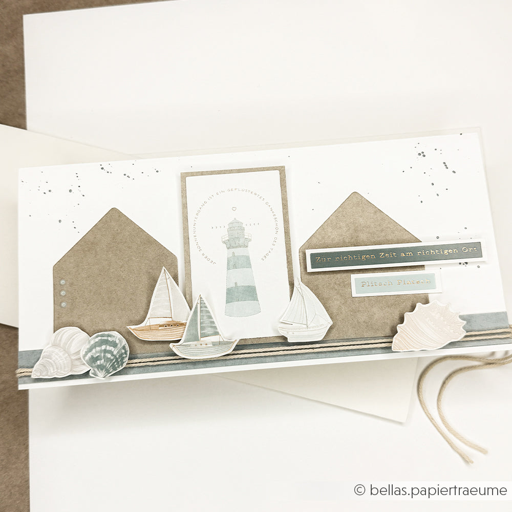 Handgemachte maritime Karte von Alexandra Renke mit Leuchtturm, Booten, Muscheln und deutschem Text - ideal für Rub-On Meeresbrise-Fans, die Motive aufbringen oder mit Transferfolien basteln möchten.