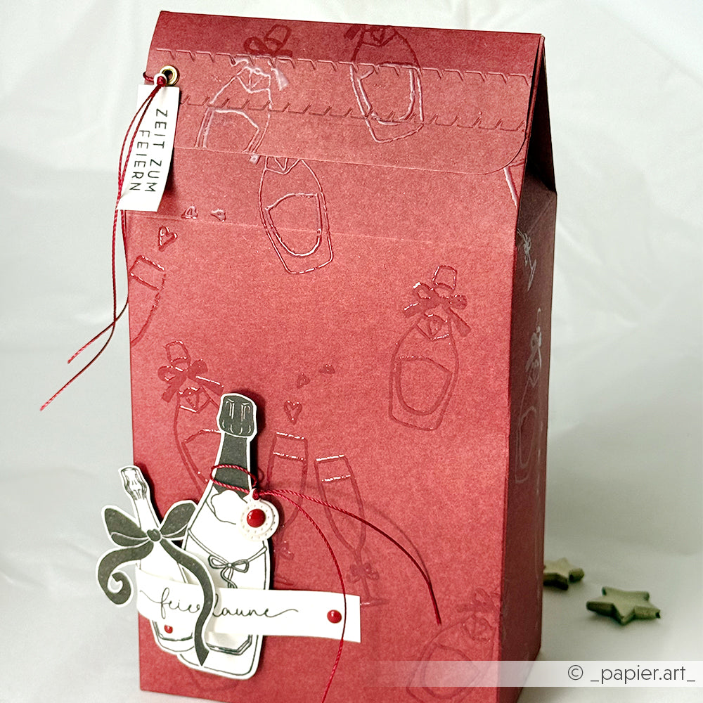 Rote Geschenktüte von Alexandra Renke mit geprägtem Sektflaschenmotiv, festlichem Anhänger, Schleife und "Zeit zum Feiern"-Etikett - ideal für Papierprojekte oder zum Aufwerten Ihrer Festtagsgeschenke mit Clear Stamp-Flair!.