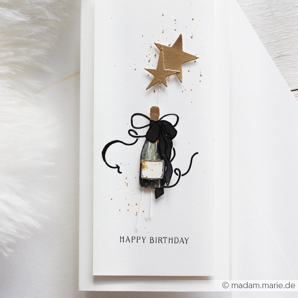 Handgefertigte Geburtstagskarte von Alexandra Renke mit einer Sektflasche, schwarzem Band, zwei goldenen Sternen, mit Photopolymer-Stempel bearbeitet und mit "Happy Birthday" abgeschlossen.