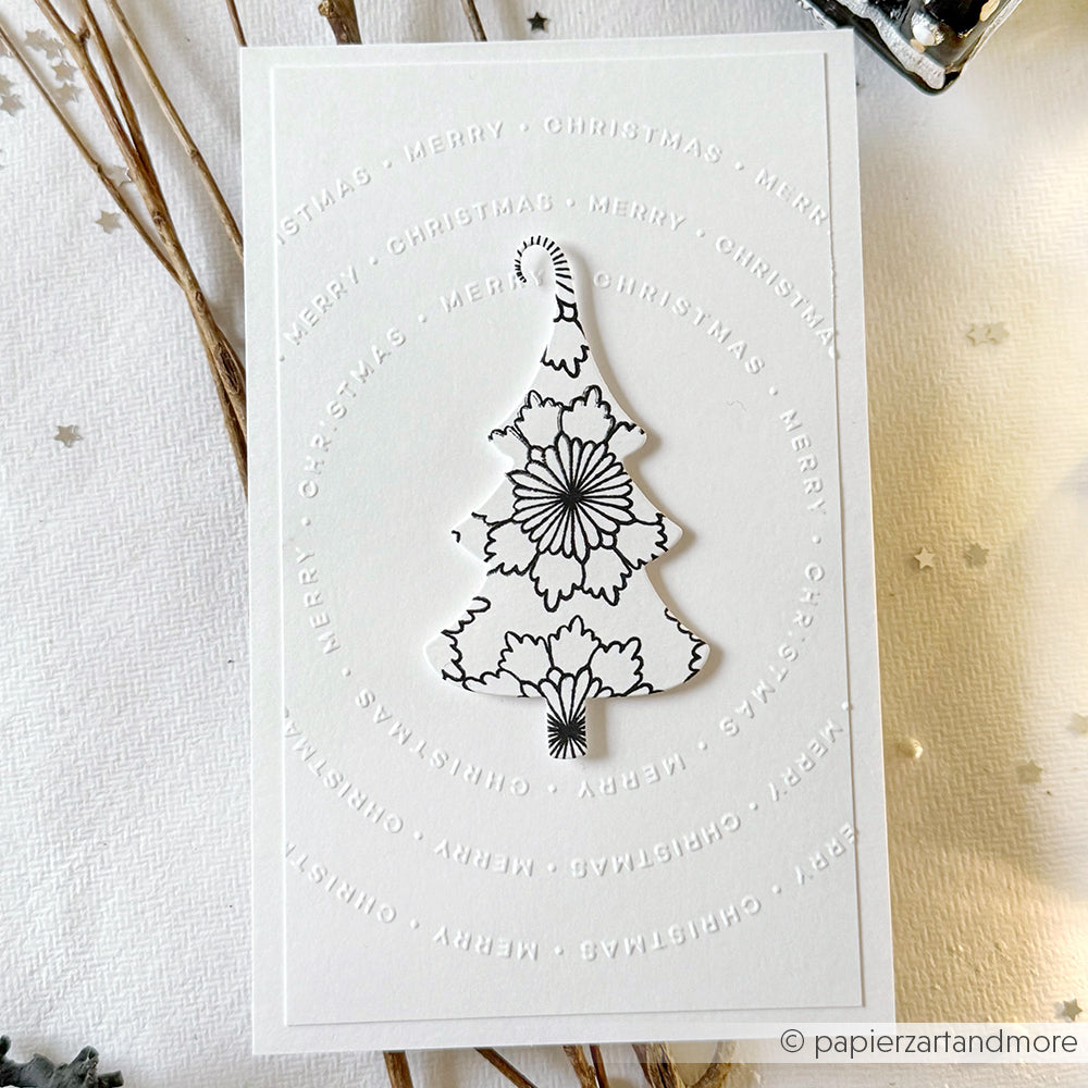 Weiße Karte mit einem schwarzen, floralen Weihnachtsbaum, gestempelt mit dem Photopolymer-Stempel von Alexandra Renke und einem kreisförmig geprägten Text "Frohe Weihnachten" - eine perfekte Kreation von Papierprojekte.