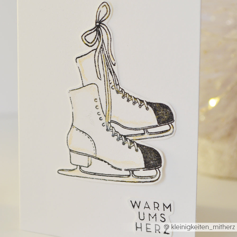 Illustration von hängenden Schlittschuhen mit "WARM UMS HERZ" auf Weiß - ideal für Kuschelzeit-Basteleien oder als klarer Alexandra Renke Photopolymer-Stempel.