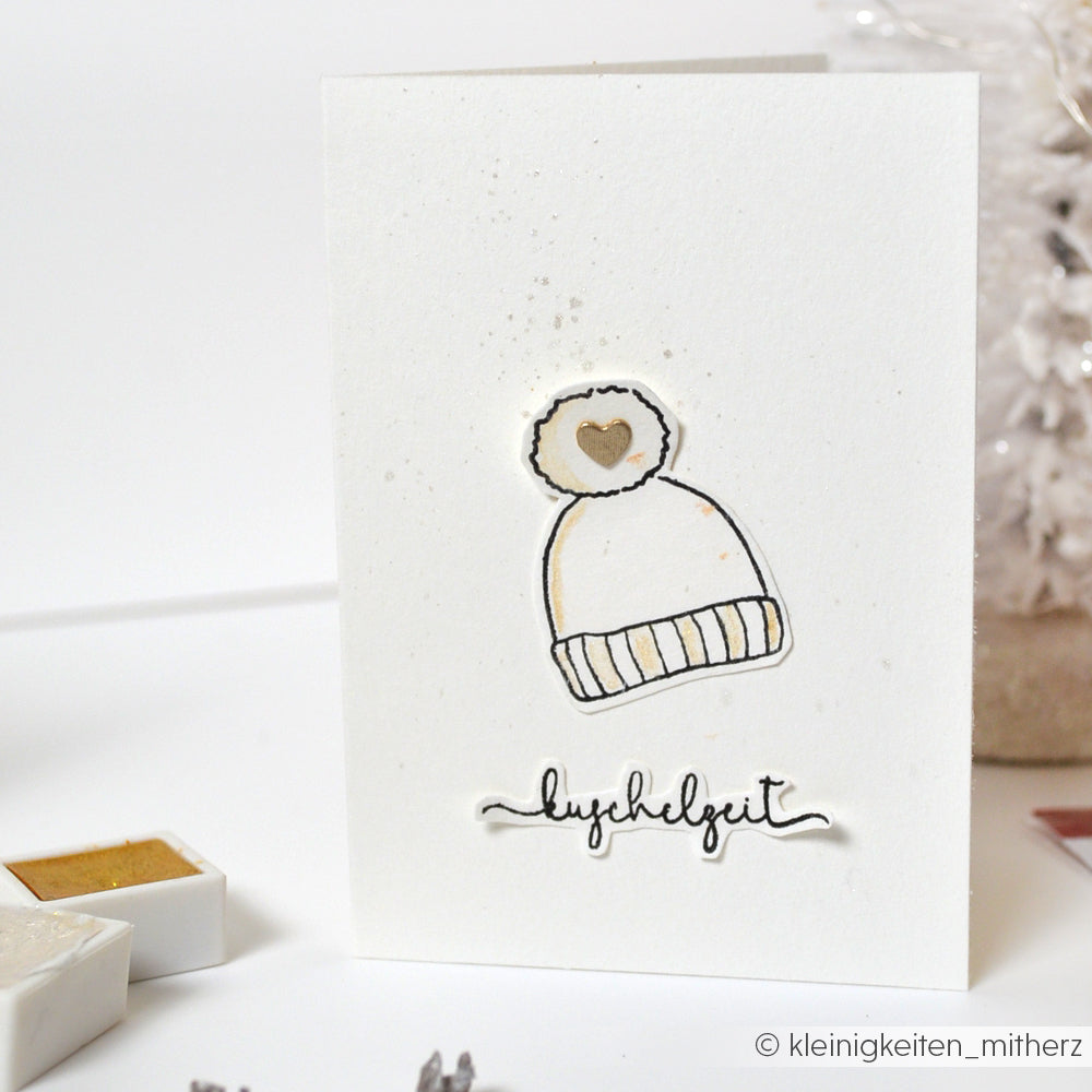 Minimalistische Karte von Alexandra Renke mit einer Illustration einer Wintermütze und "Kuschelzeit" darunter, ideal zum Stempeln mit Ihrem Lieblings-Photopolymer-Klarsichtstempel.