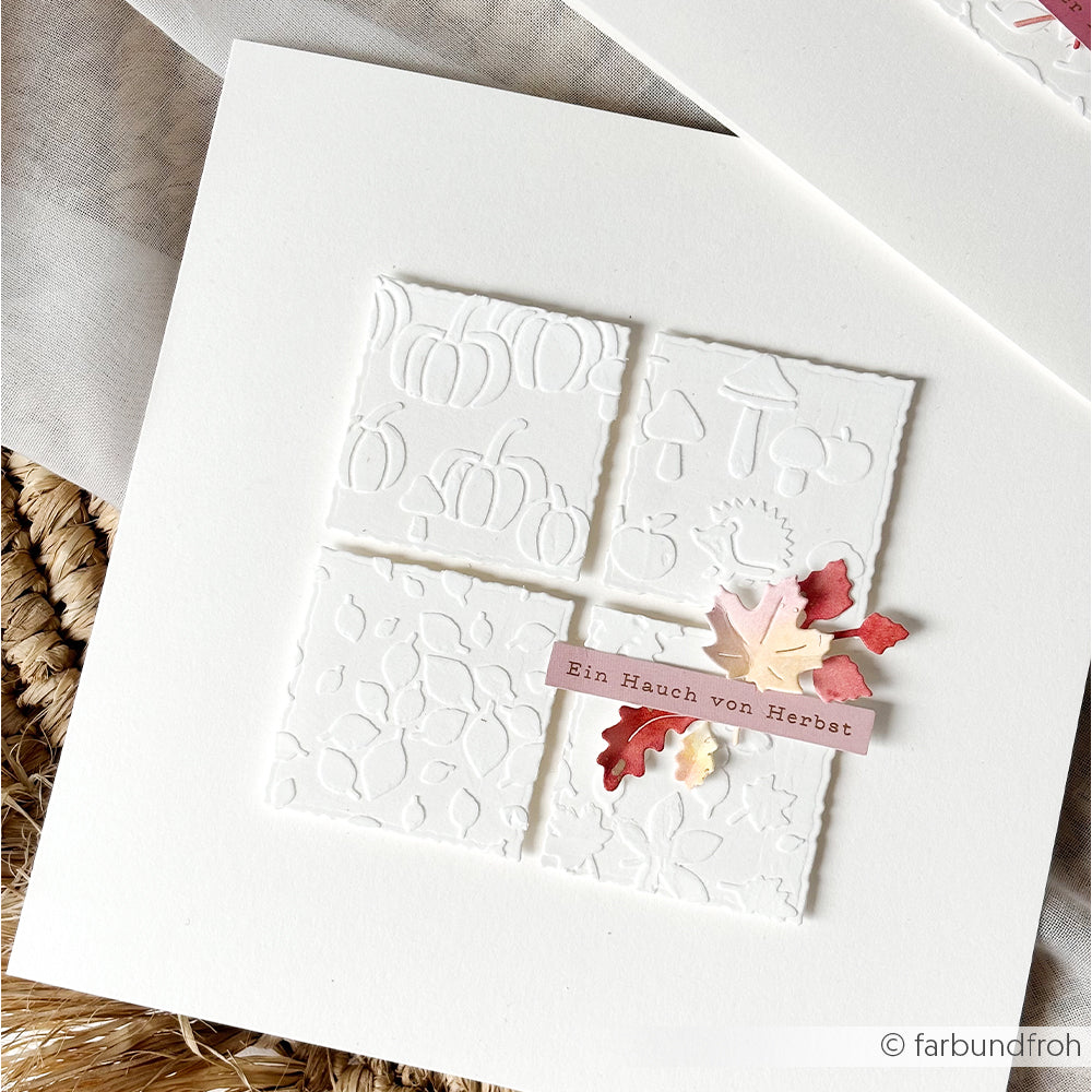 Weiße Karte mit geprägten Herbstmotiven, Papierblättern und einem Etikett mit der Aufschrift „Ein Hauch von Herbst“. Diese wiederverwendbaren Schablonen aus der Serie „Herbstfreuden“ sorgen mit ihren filigranen saisonalen Details für einen bezaubernden handgemachten Touch.