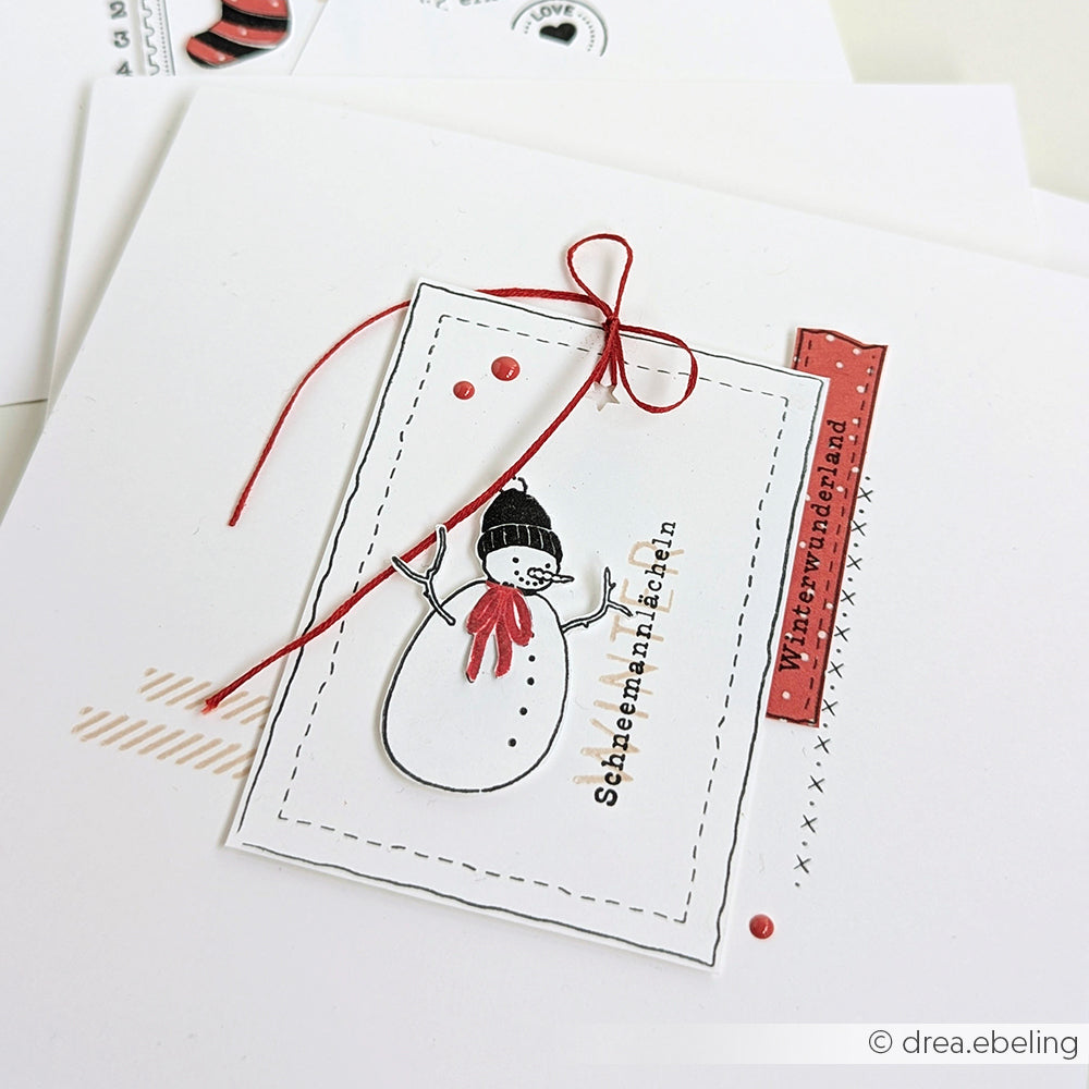 Handgefertigte Karte von Alexandra Renke mit einer Schneemannzeichnung, roter Schnur und dem deutschen Text "Schneemannlächeln" und "Winterwunderland", hergestellt mit einem Clear Stamp für klare Linien.