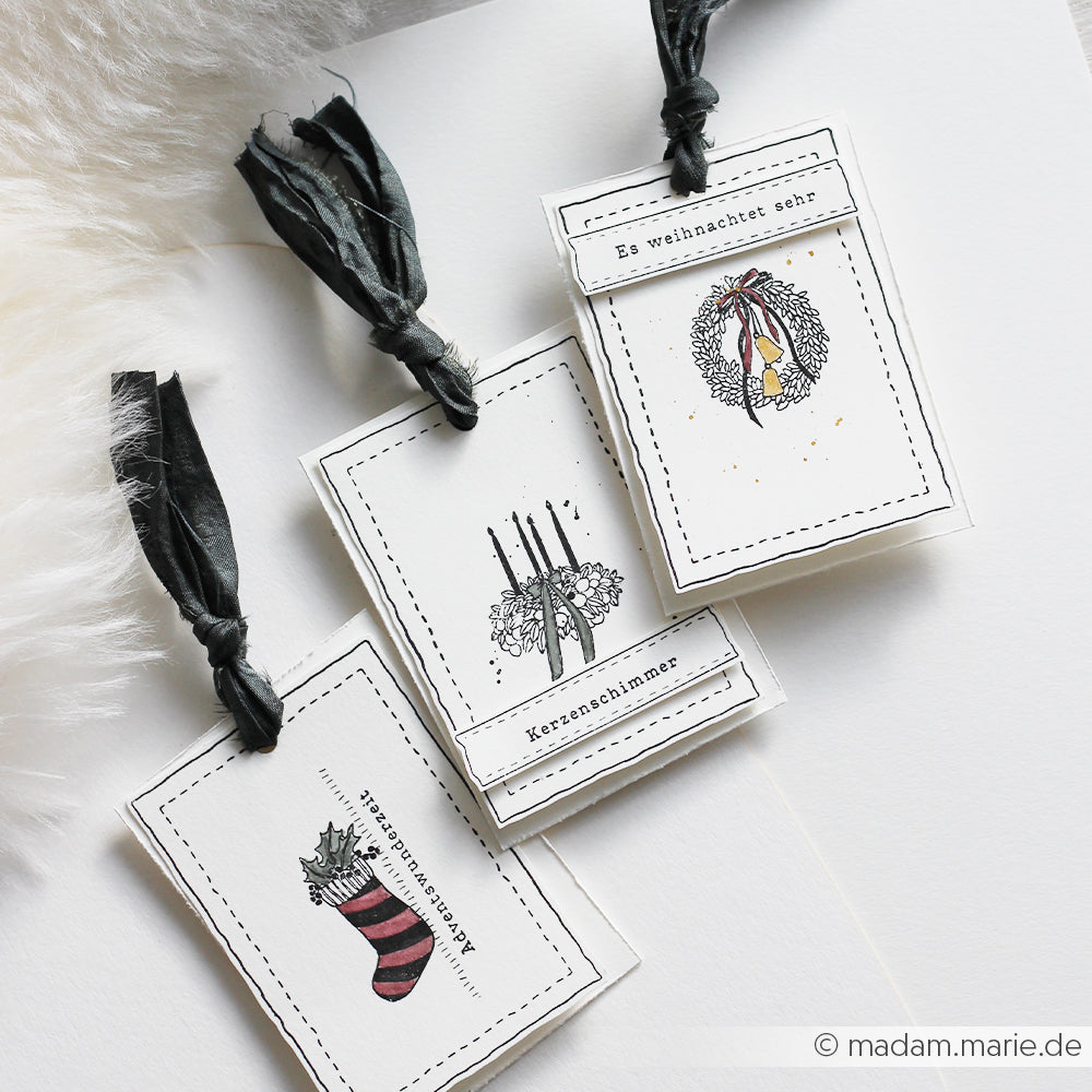 Drei handgefertigte Weihnachtsgeschenkanhänger von Alexandra Renke, die mit festlichen Illustrationen von Clear Stamp gestaltet und mit schwarzen Bändern verziert sind.