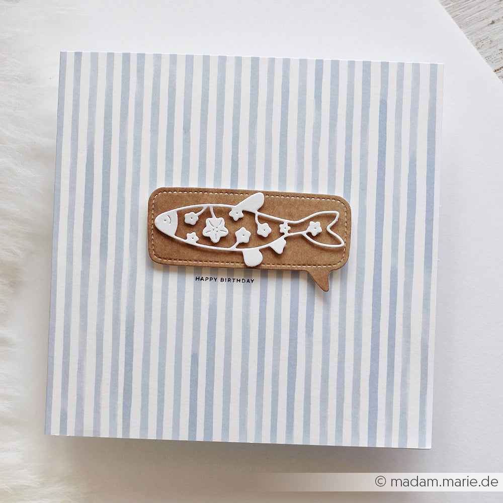 Gestreifte Karte mit einem braunen Fischausschnitt und dem Schriftzug „HAPPY BIRTHDAY“ auf weißem Hintergrund. Gestaltet mit „Stanzen für Designpapiere“ und „DieCut Systeme“ für präzise Formen und klare Linien.