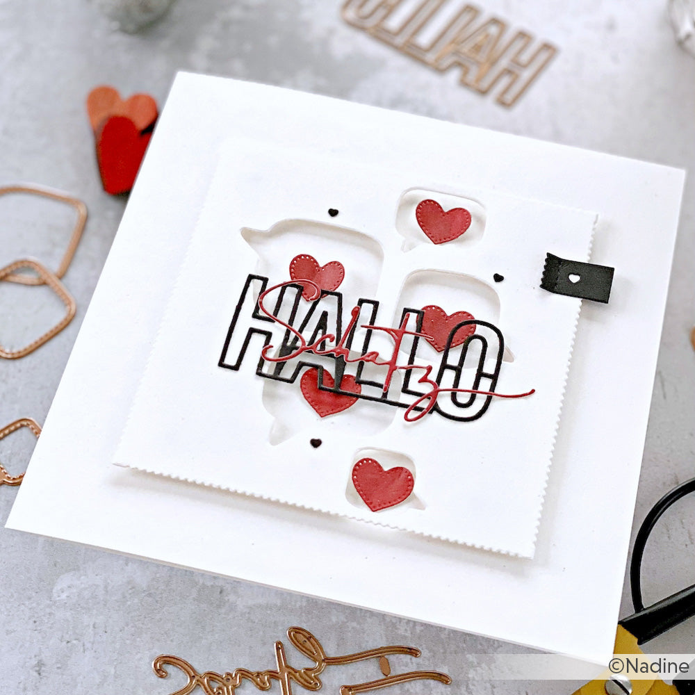 Eine handgefertigte Grußkarte von Alexandra Renke mit roten Herzen, "HALLO"- und "Hallo"-Schriftzug sowie Akzenten aus Motivstanze Kleine Sprechblasen Links auf Designpapier, alles vor weißem Hintergrund.