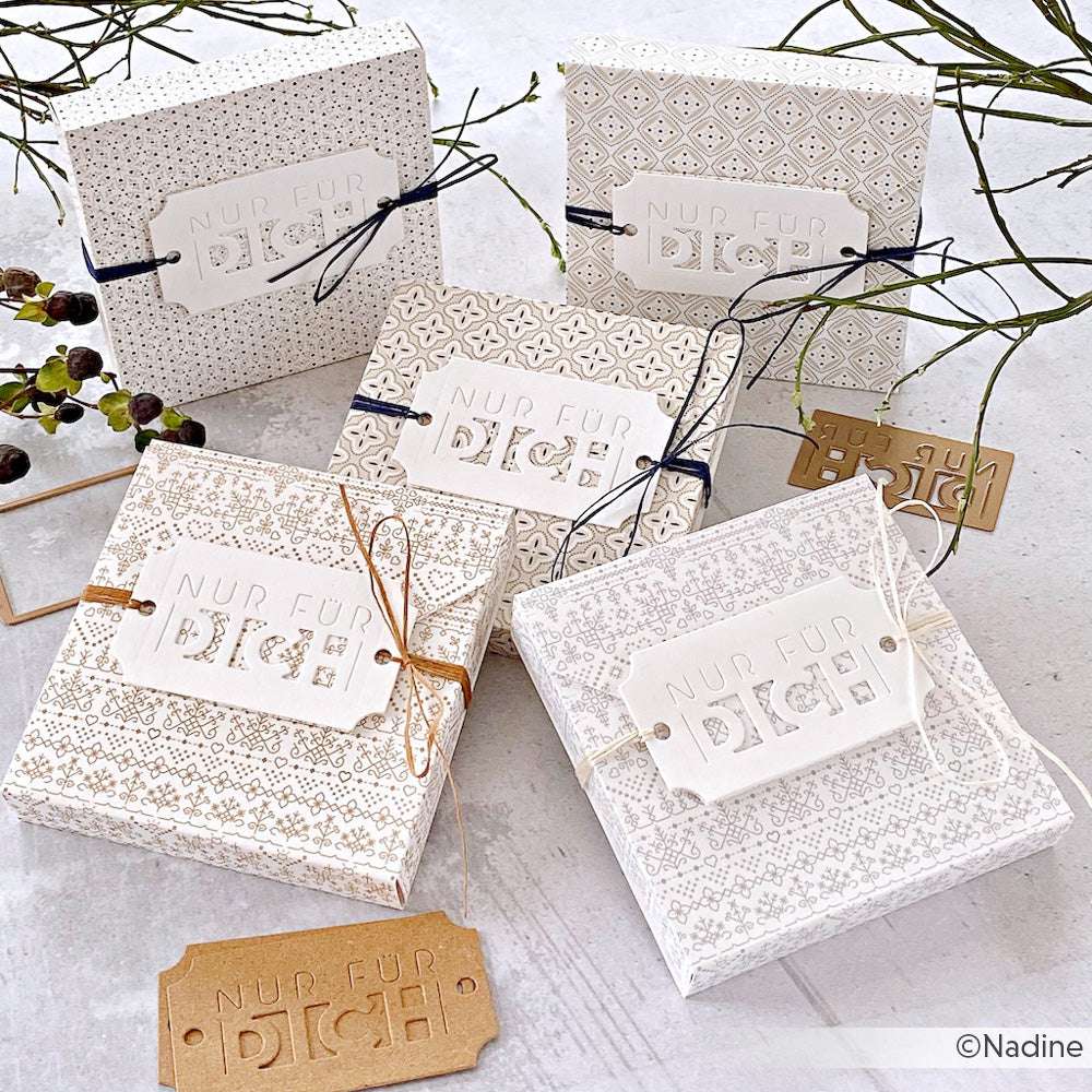 Fünf gemusterte Geschenkboxen von Alexandra Renke, jede mit einer Schnur verschnürt und mit der Aufschrift "Nur für Dich" versehen, aus stilvollen Designpapieren gefertigt und auf einer weißen Fläche präsentiert.