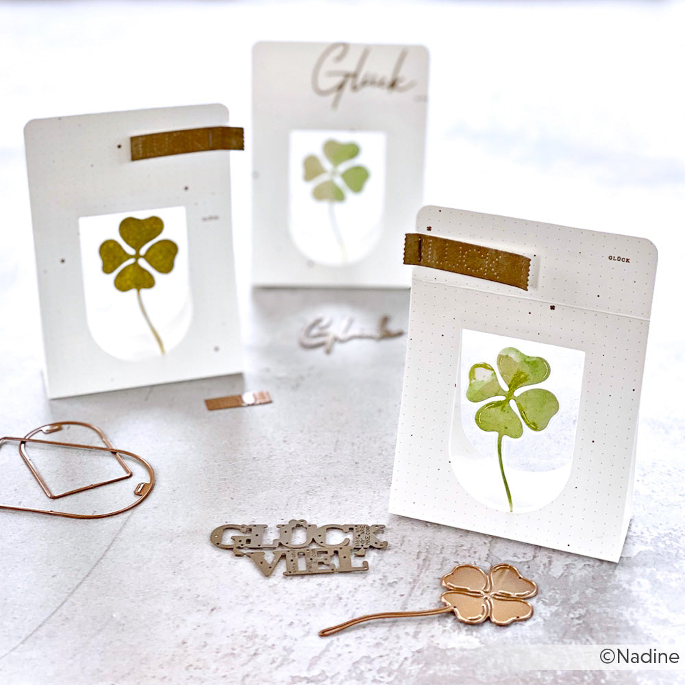 Drei handgefertigte Karten aus dem Set Kleeblätter von Alexandra Renke mit vierblättrigen Kleeblättern und goldenen Akzenten, die mit Motivstanze Dies hergestellt wurden, werden auf einer hellen Oberfläche wunderschön präsentiert.