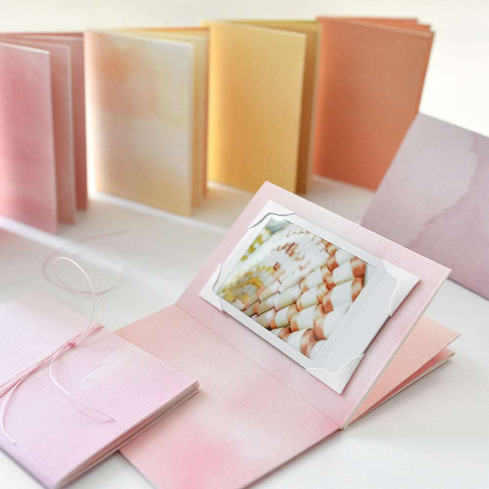 Pastellfarbene Fotoalben von Alexandra Renke, mit einem aufgeschlagenen Album mit Muschelfoto im Inneren, kreativ dekoriert mit dem Fotoecken-Set und passenden Designpapieren für mehr Flair.