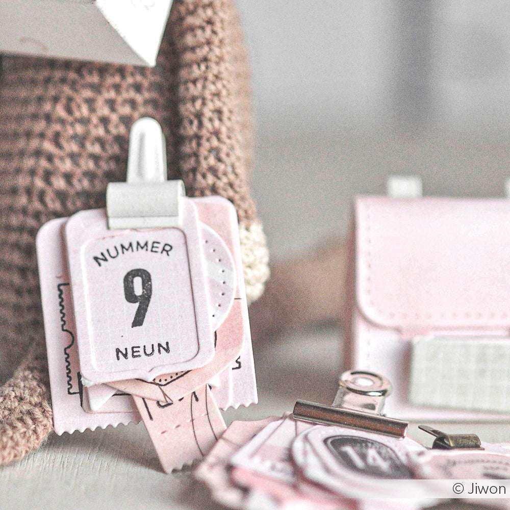 Die Nahaufnahme eines kleinen Papierkalenders von Alexandra Renke zeigt die Zahl 9 und das Wort NUMMER NEUN, gestaltet mit eleganten Designpapieren für einen stilvollen Touch.