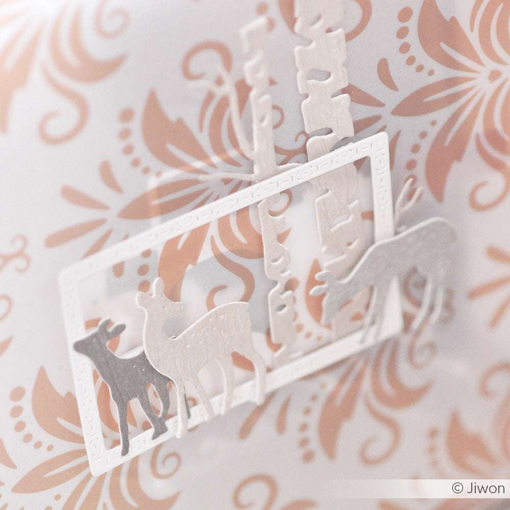 Weißer Papierausschnitt mit zwei Rehen und Bäumen auf einem dekorativen, floral gemusterten Hintergrund, hergestellt mit präzisen Stanzen für Designpapier mit Alexandra Renke DieCut Systemen.