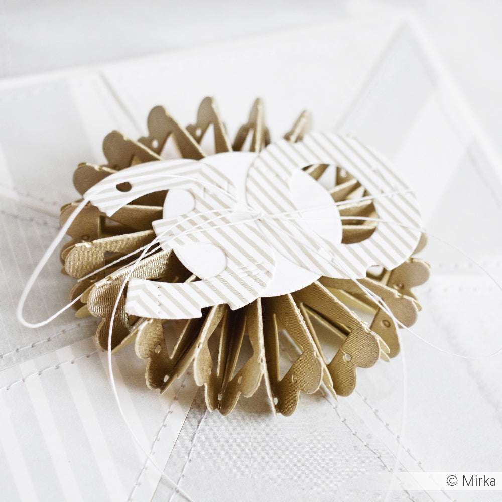 Goldfarbene und weiße Papierrosette mit der Alexandra Renke Motivstanze Rosette, gekrönt mit der Zahl 50, auf weißem, strukturiertem Hintergrund.