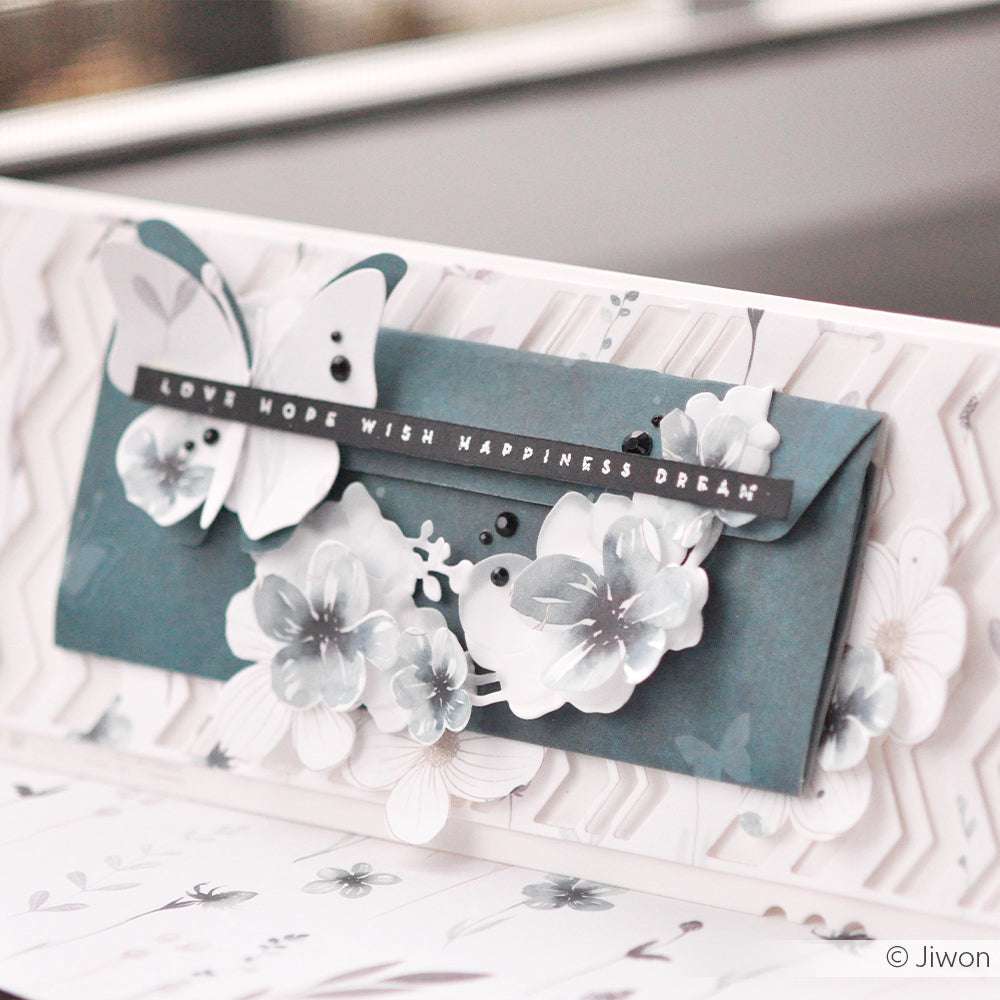 Blauer Umschlag von Alexandra Renke mit 3D-Blumen, einem Schmetterling und dem Schriftzug LOVE HOPE WISH HAPPINESS DREAM - hergestellt mit Designpapieren und DieCut Systemen für eine detaillierte Dekoration.