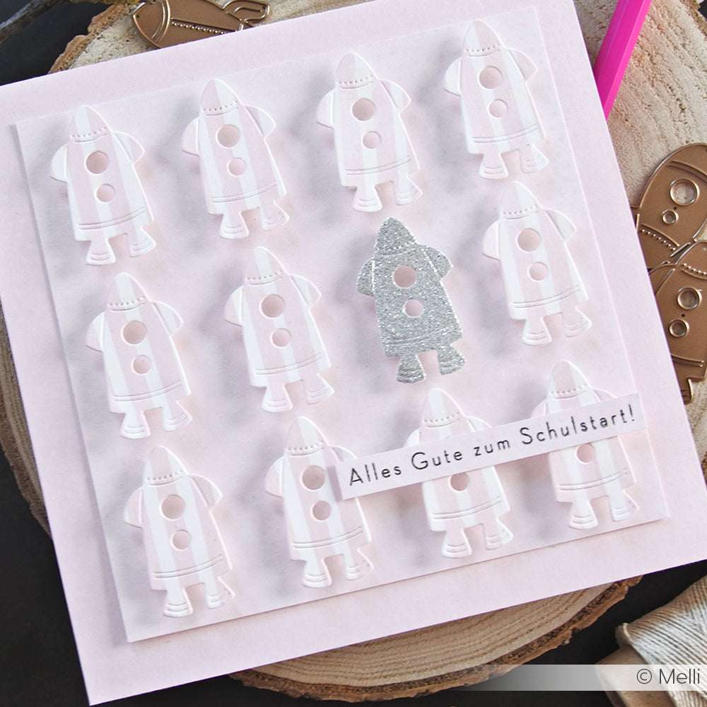 Rosafarbene Karte mit weißen Raketen und einer einzelnen Glitzerrakete, hergestellt mit der Motivstanze 3 Raketen von Alexandra Renke; mit dem Gruß "Alles Gute zum Schulstart!".