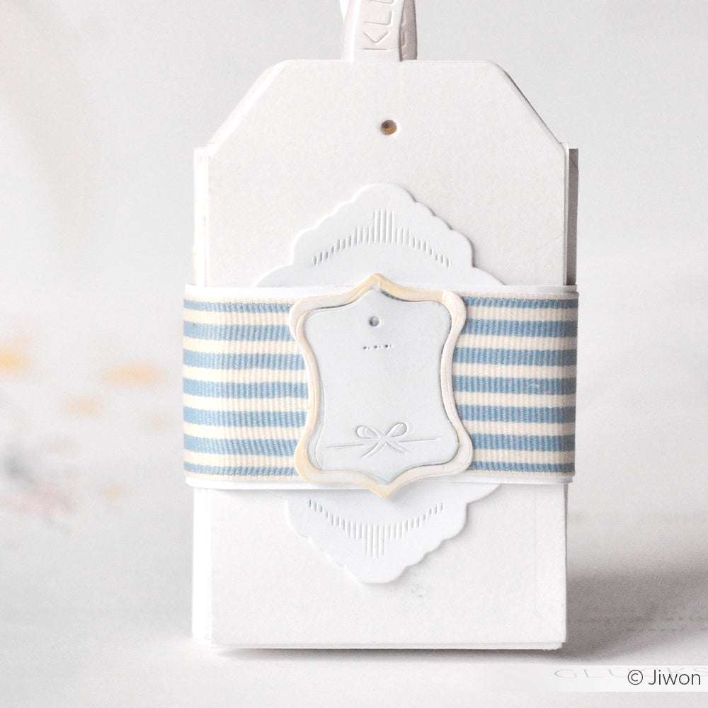Weißer Geschenkanhänger von Alexandra Renke, umwickelt mit blau-weiß gestreiftem Band, kleinem Rahmen und Schleifendetail, hergestellt mit der Motivstanze Etikett Vic 1 für präzise Kanten.