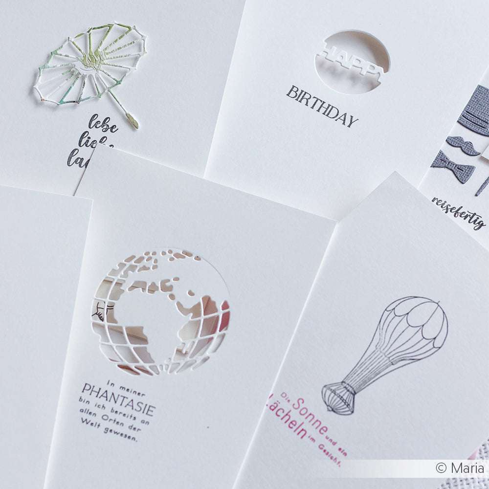 Ein Set weißer Grußkarten von Alexandra Renke mit zarten ausgeschnittenen und gedruckten Globus-, Ballon- und Sonnenschirm-Motiven auf exquisitem Designerpapier.