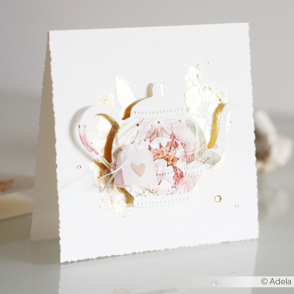 Weiße Grußkarte von Alexandra Renke mit einem floralen Teekannenmotiv aus der Motivstanze Teekanne DieCut Systeme und goldenen Akzenten auf der Vorderseite, aufrecht stehend.