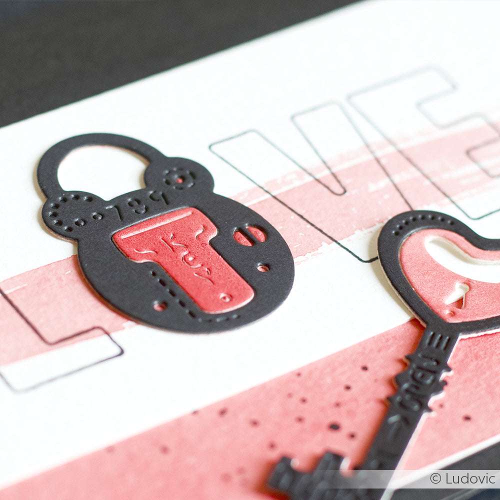Nahaufnahme einer Karte, die mit der Motivstanze Schloss Vic von Alexandra Renke gestaltet wurde. Sie zeigt gestanzte Schloss- und Schlüsselformen über den Buchstaben LOVE in rosa und schwarzen Designpapieren.