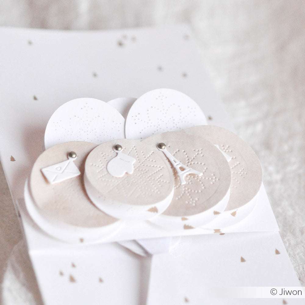 Weiße Papierkarte von Alexandra Renke mit runden, geprägten Fäustlings-, Buchstaben- und Eiffelturm-Motiven - ideal für die Verwendung mit der Motivstanze oder dem Mini-Anhänger-Set DieCut Systeme.