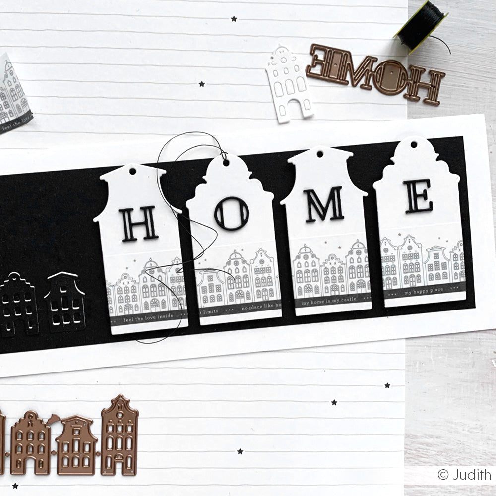 Vier weiße Anhänger von Alexandra Renke mit HOME-Buchstaben, Stadtmustern und dekorativen Stanzungen liegen auf liniertem Papier mit stilvollem Designpapier.