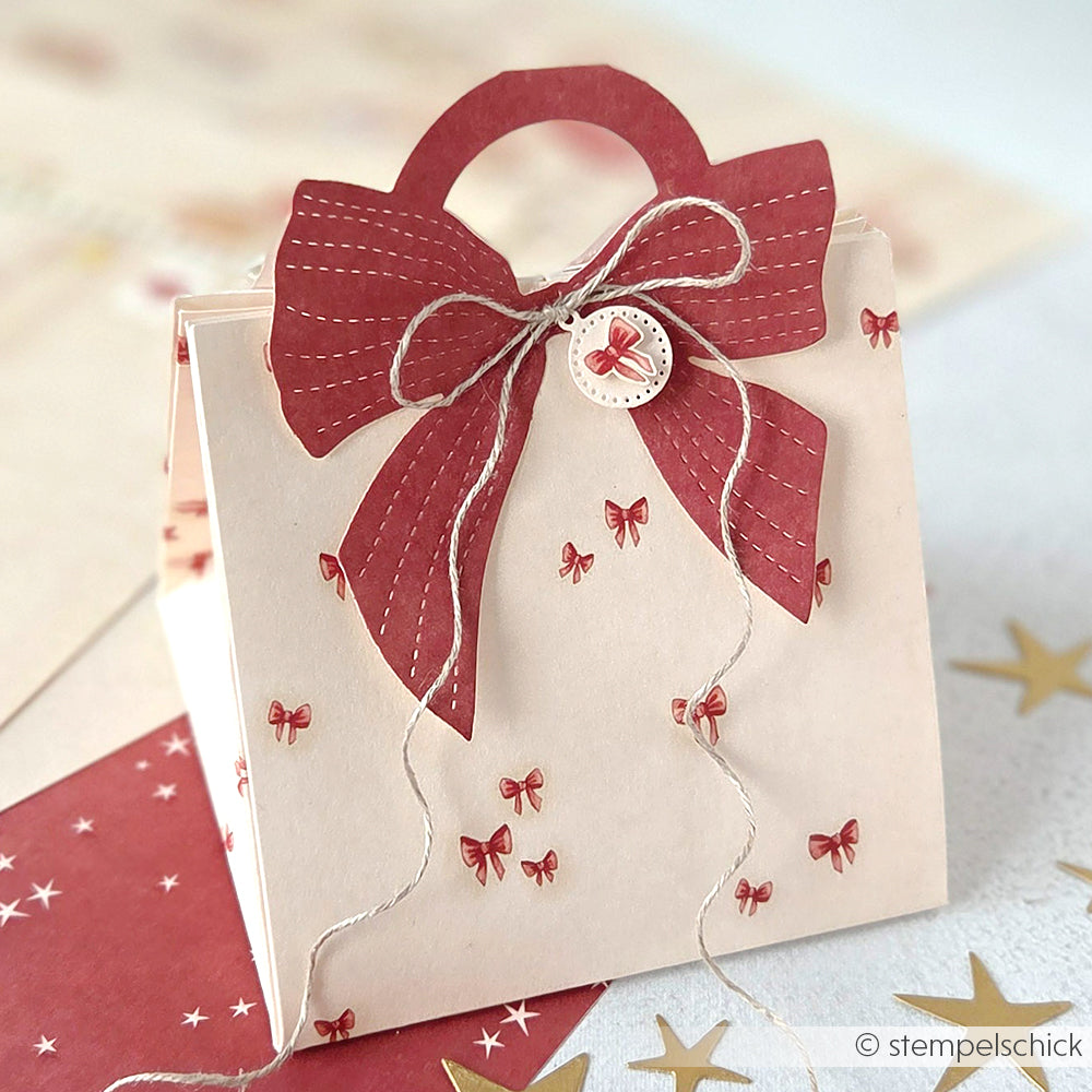 Cremefarbene Geschenktüte mit roten Schleifen, einer großen roten Schleife oben und Bindfaden am Henkel - gefertigt mit Alexandra Renke Motivstanze Tütengriff Schleife und eleganten Designpapieren für eine stilvolle, festliche Note.