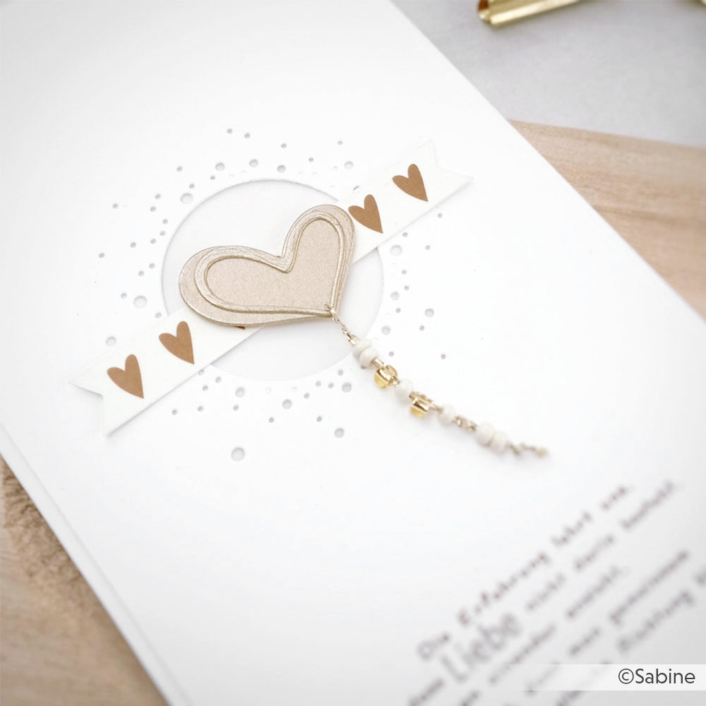 Handgefertigte Karte von Alexandra Renke, hergestellt aus hochwertigem Designpapier, mit einem beigen Herz, goldenen Perlen und einem weißen Banner mit goldenen Herzen auf einem weißen Hintergrund.